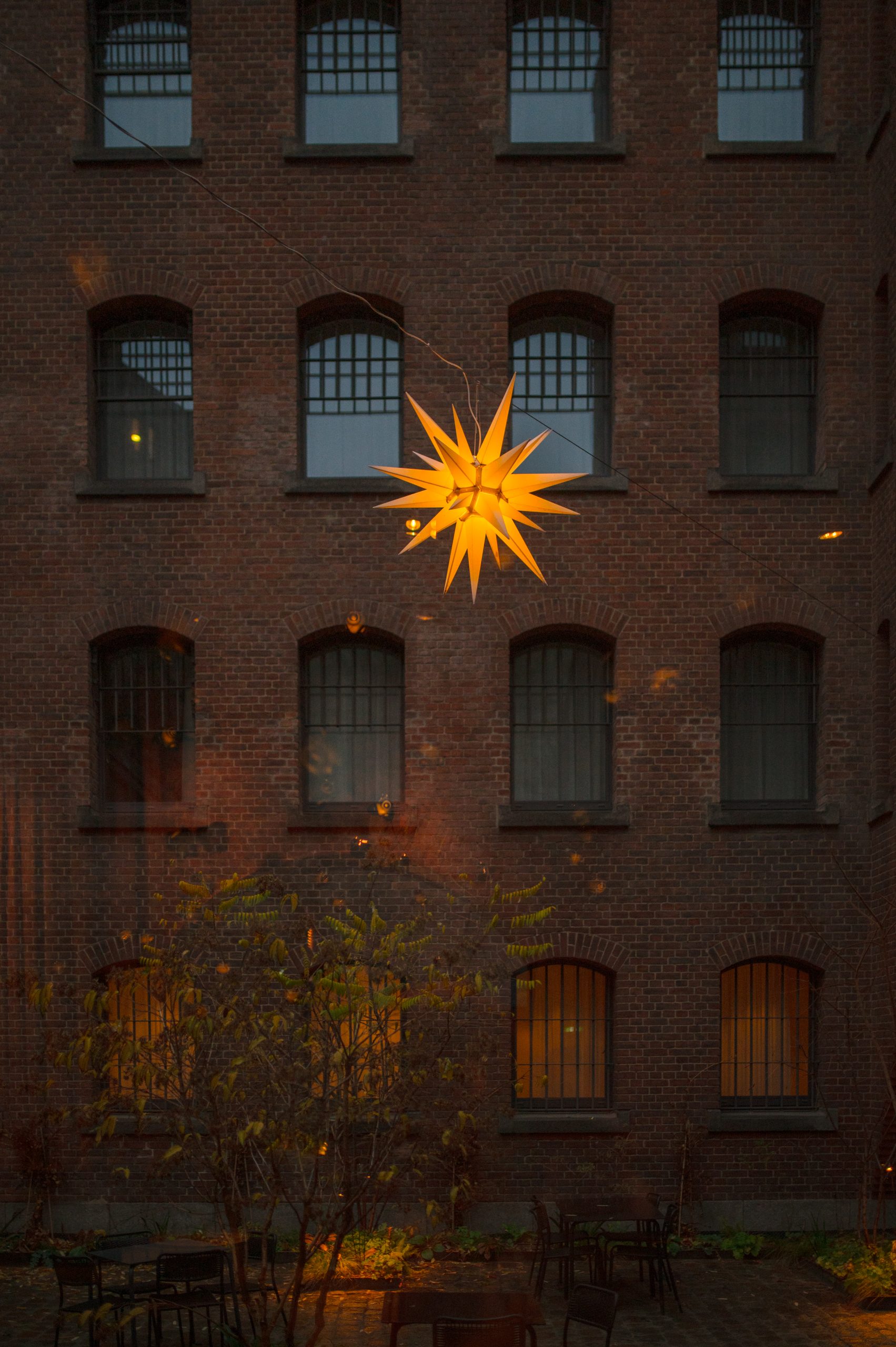 Hängende Weihnachtsstern-Lampe vor rotem Backstein-Gebäude.